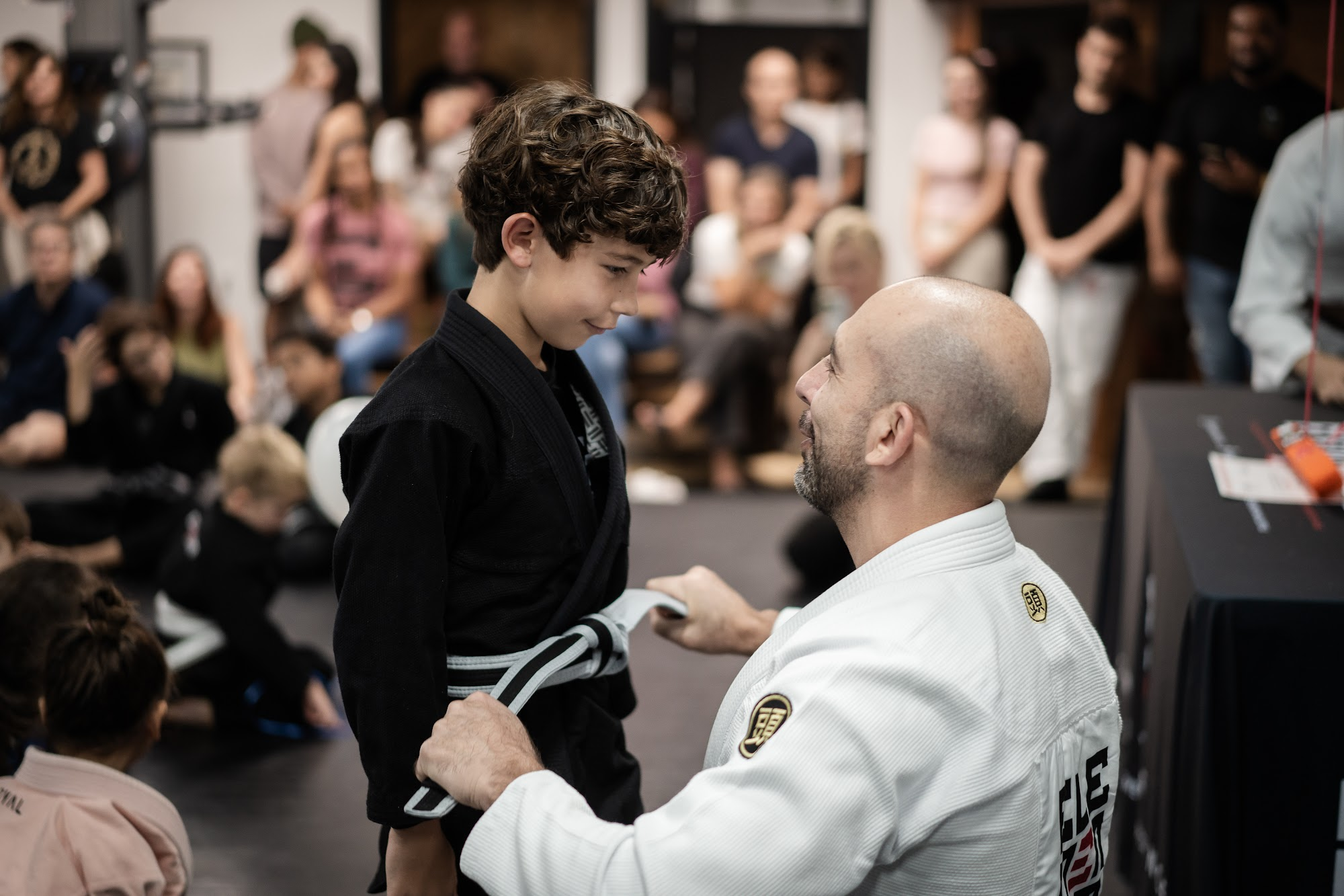 Coach tying a belt on a young student during a Kids 2 Jiu-Jitsu class at Elementum